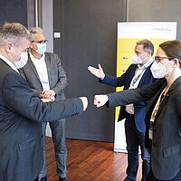 Eine Gruppe von Menschen steht zusammen und trägt eine Maske, Franz Loogen steht ebenfalls in der Gruppe und begrüßt die Teilnehmenden vor Ort. 