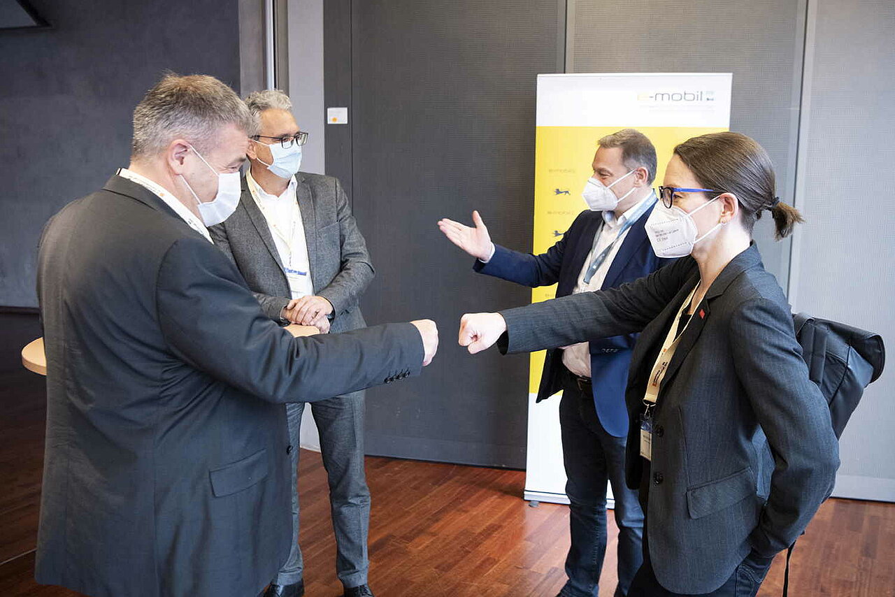 Eine Gruppe von Menschen steht zusammen und trägt eine Maske, Franz Loogen steht ebenfalls in der Gruppe und begrüßt die Teilnehmenden vor Ort. 