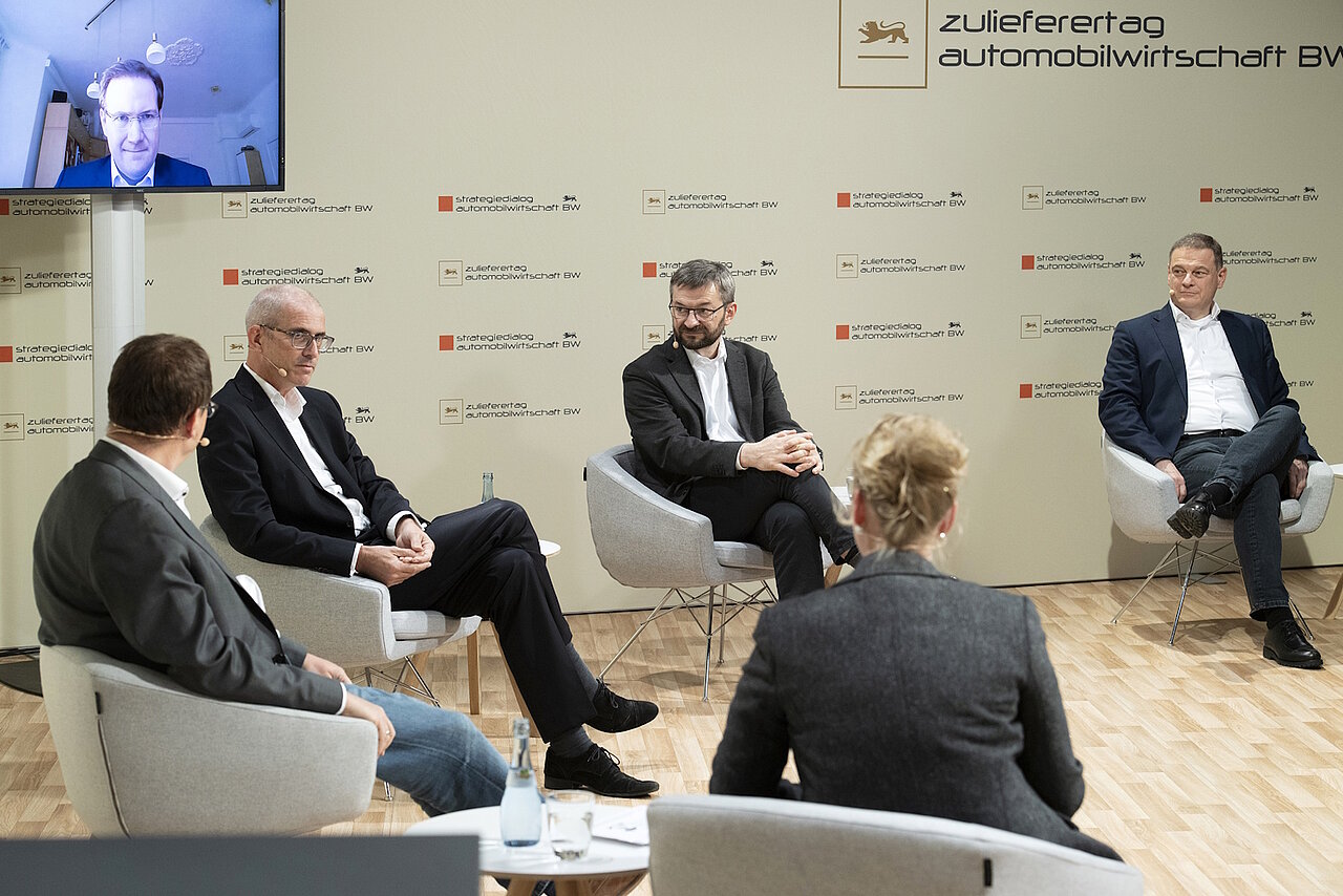 Die Podiumsteilnehmenden am Zulieferertag Automobilwirtschaft BW 2020 sitzen im Halbkreis, im Hintergrund ist ein Referent per Video zugeschaltet.