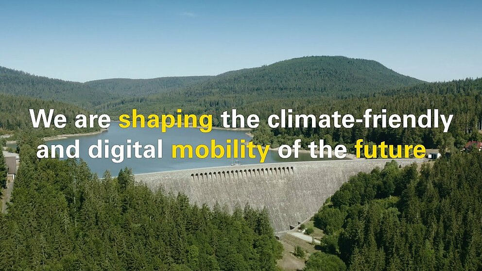 Das Thumbnail des englischen YouTube Videos zum Cluster Elektromobilität Süd-West. Es ist ein Stausee zu sehen, im Vordergrund steht der Text "We are shaping the climate friendly and digital mobility of the future".