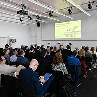 Ein gefüllter Veranstaltungssaal mit vielen Menschen. Auf dem Podium steht der Verkehrsminister Winfried Hermann.