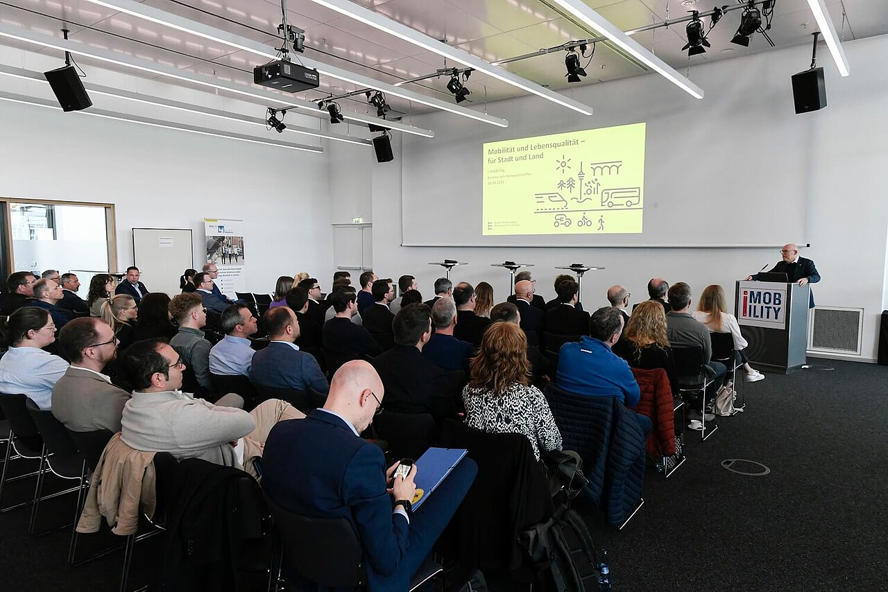 Ein gefüllter Veranstaltungssaal mit vielen Menschen. Auf dem Podium steht der Verkehrsminister Winfried Hermann.