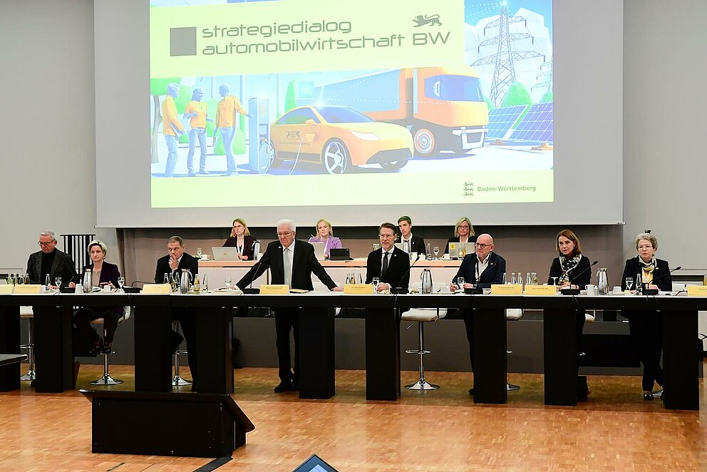 Ministerpräsident Winfried Kretschmann eröffnet das Top-Level-Meeting. auf dem Strategiedialog Automobilwirtschaft BW. Er ist umgeben von anderen wichtigen Vertreter:innen der Industrie.