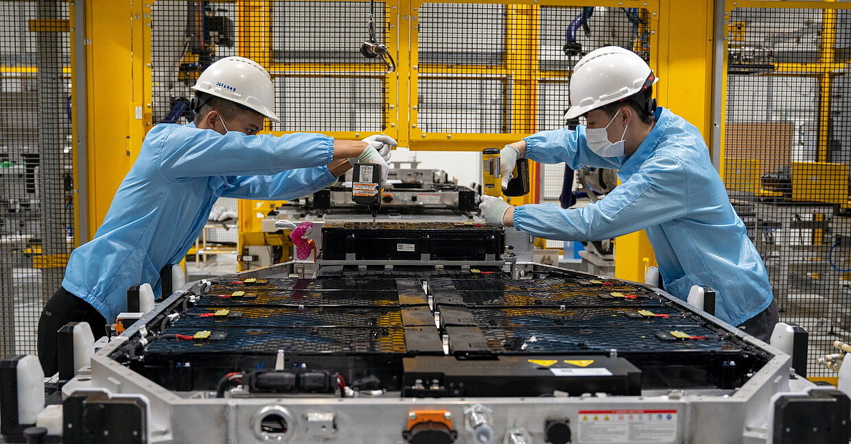 Zwei Menschen arbeiten in einer Fabrik an einer Batterie für Elektrofahrzeuge.