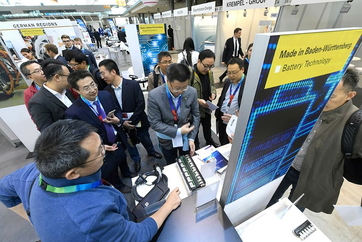 Ein Stand auf einer Messe, mehrere Menschen stehen um den Stand herum.