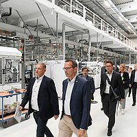 Eine Besuchergruppe läuft durch eine Fabrikhalle mit Testständen für Brennstoffzellenstacks.