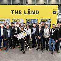 Eine Gruppe von Menschen vor einer gelbes Messewand auf der Hannover Messe.