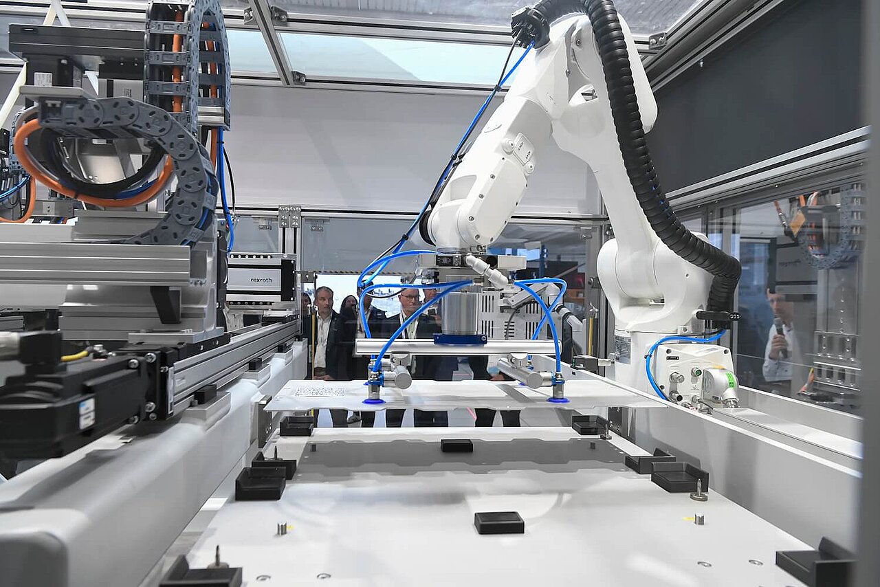 Produktionsanlage für Batteriepacks. Interessierte Personen blicken auf einen Roboterarm.