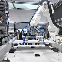 Produktionsanlage für Batteriepacks. Interessierte Personen blicken auf einen Roboterarm.