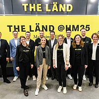 Gruppenfoto mit Mitarbeiterinnen und Mitarbeitern der e-mobil BW GmbH am Messestand von THE LÄND auf der Hannover Messe.