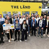 Eine Gruppe von Menschen vor einer gelbes Messewand auf der Hannover Messe.