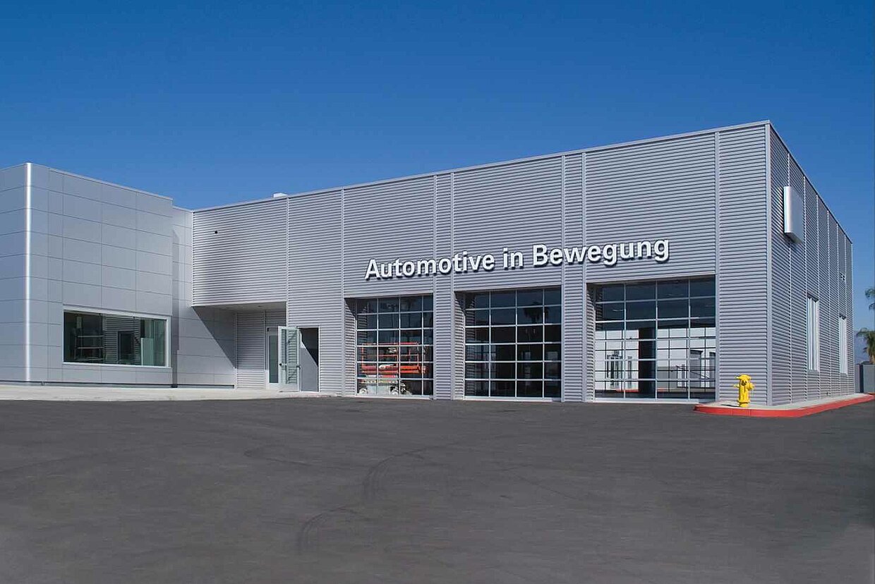 Autohaus "Automotive in Bewegung" Ansicht eines Autohauses von Außen. Über der Garage steht "Automotive in Bewegung"