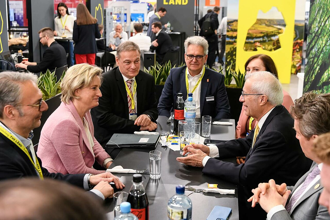 Dr. Nicole Hoffmeister-Kraut ist im Gespräch und sitzt mit mehreren Personen an einem Tisch. Im Hintergrund der THE LÄND-Messestand auf der Hannover Messe.