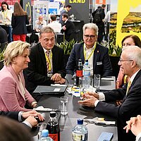 Dr. Nicole Hoffmeister-Kraut ist im Gespräch und sitzt mit mehreren Personen an einem Tisch. Im Hintergrund der THE LÄND-Messestand auf der Hannover Messe.