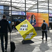 Außenaufnahme auf der Hannover Messe. Ein gelber Würfel in den Baden-Württemberg-Farben weist auf den THE LÄND-Pavillon hin.