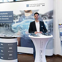 Ein Informationsstand der Landeslotsenstelle Transformationswissen BW mit Tisch und Aufsteller, dahinter steht Tim Siegel der e-mobil BW.