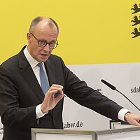 Bundeskanzler Friedrich Merz bei der Pressekonferenz des Strategiedialog Automobilwirtschaft BW vor einer gelben Wand.