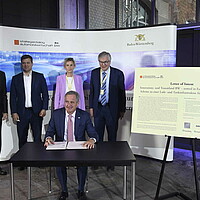 Ministerpräsident Kretschmann gemeinsam mit Wirtschaftsvertreter:innen unterzeichnen eine Absichtserklärung für ein „Pilot-Lade- und Wasserstoff-Tankinfrastrukturprojekt für Langstrecken-Lkw“.