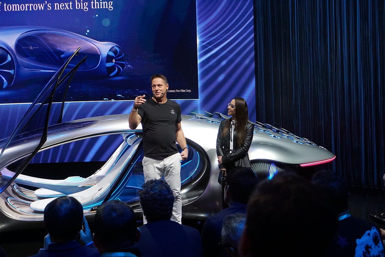 Show eines neuen Konzeptfahrzeug auf der Messe. Im Vordergrund spricht ein Referent lebendig von neuen Design und Funktionen des Autos.