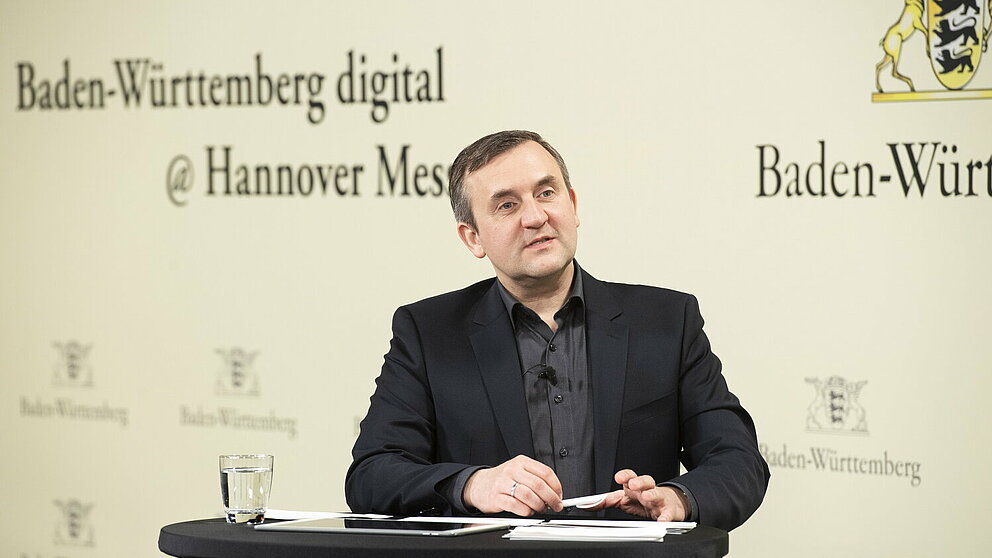 Wolfgang Fischer steht vor einem Rednerpult und spricht, im Hintergrund ist eine Messewand mit der Aufschrift "Baden-Württemberg digital @ Hannover Messe" zu sehen.