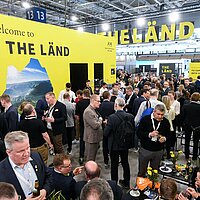 Ein gut befüllter Messestand mit mehreren Menschen, die sich auf dem THE LÄND-Pavillon austauschen.