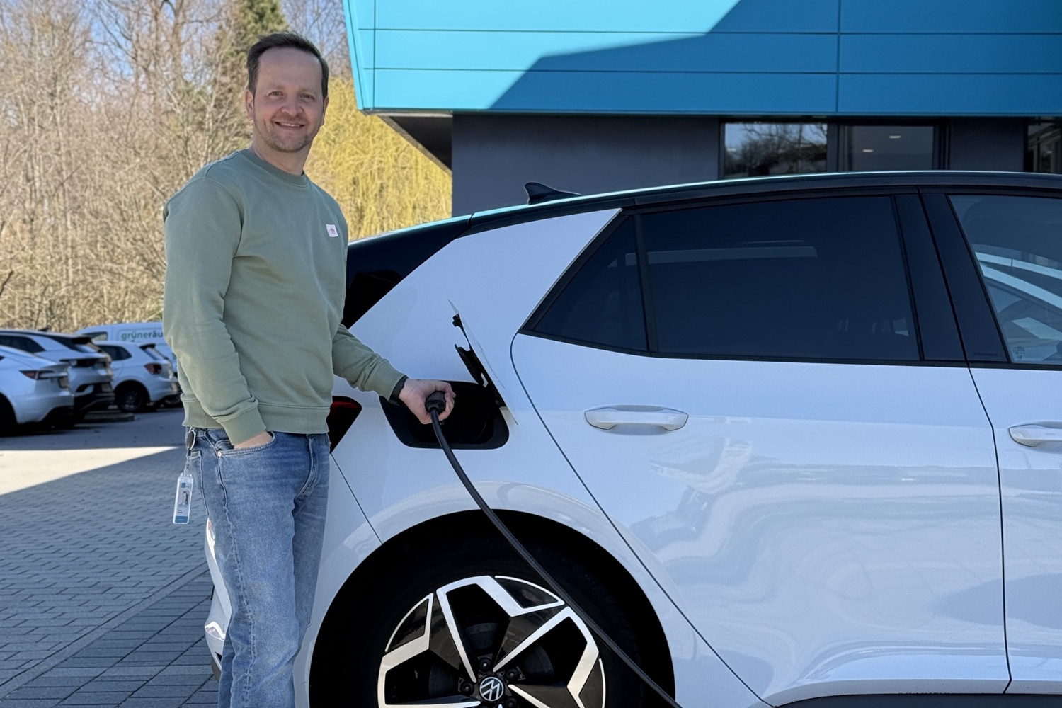 Ein Mann steht neben einem weißen Elektroauto und steckt den Ladestecker ein.