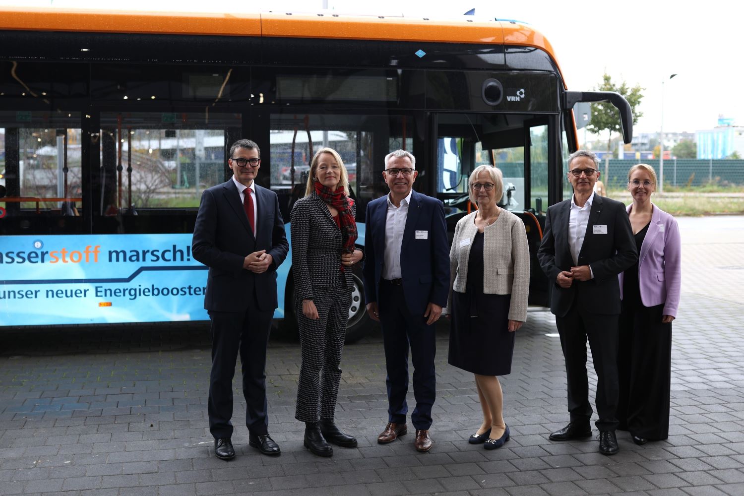 Sechs Personen vor einem mit Wasserstoff betriebenen Stadtbus.